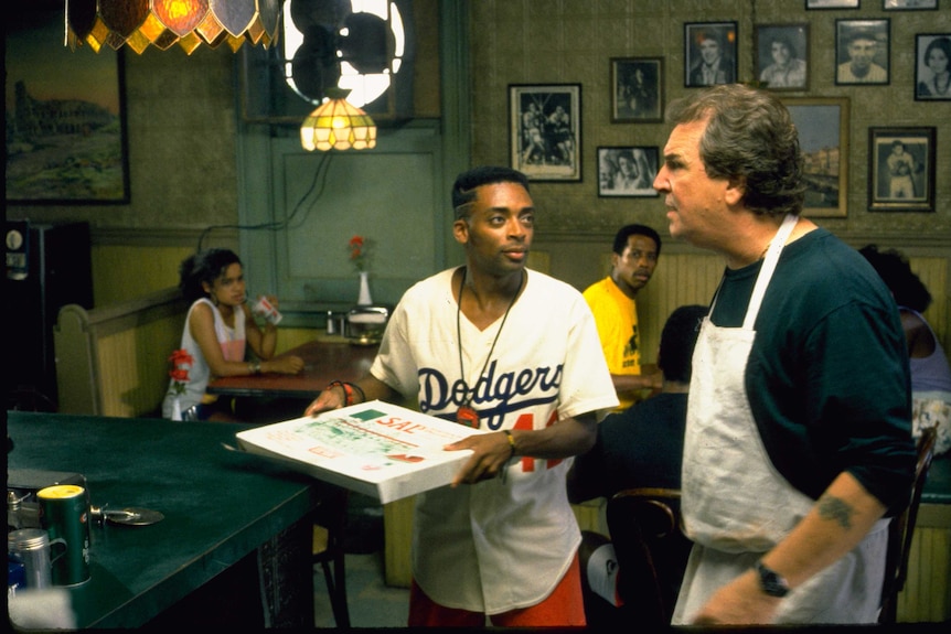 A scene from the film Do The Right Thing with Spike Lee holding a pizza talking to a cook (played by Danny Aiello)