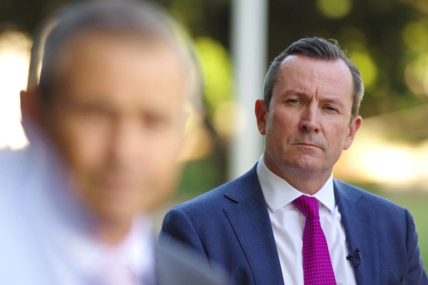 WA Premier Mark McGowan stands in the distance watching the Health Minister brief reporters on coronavirus.