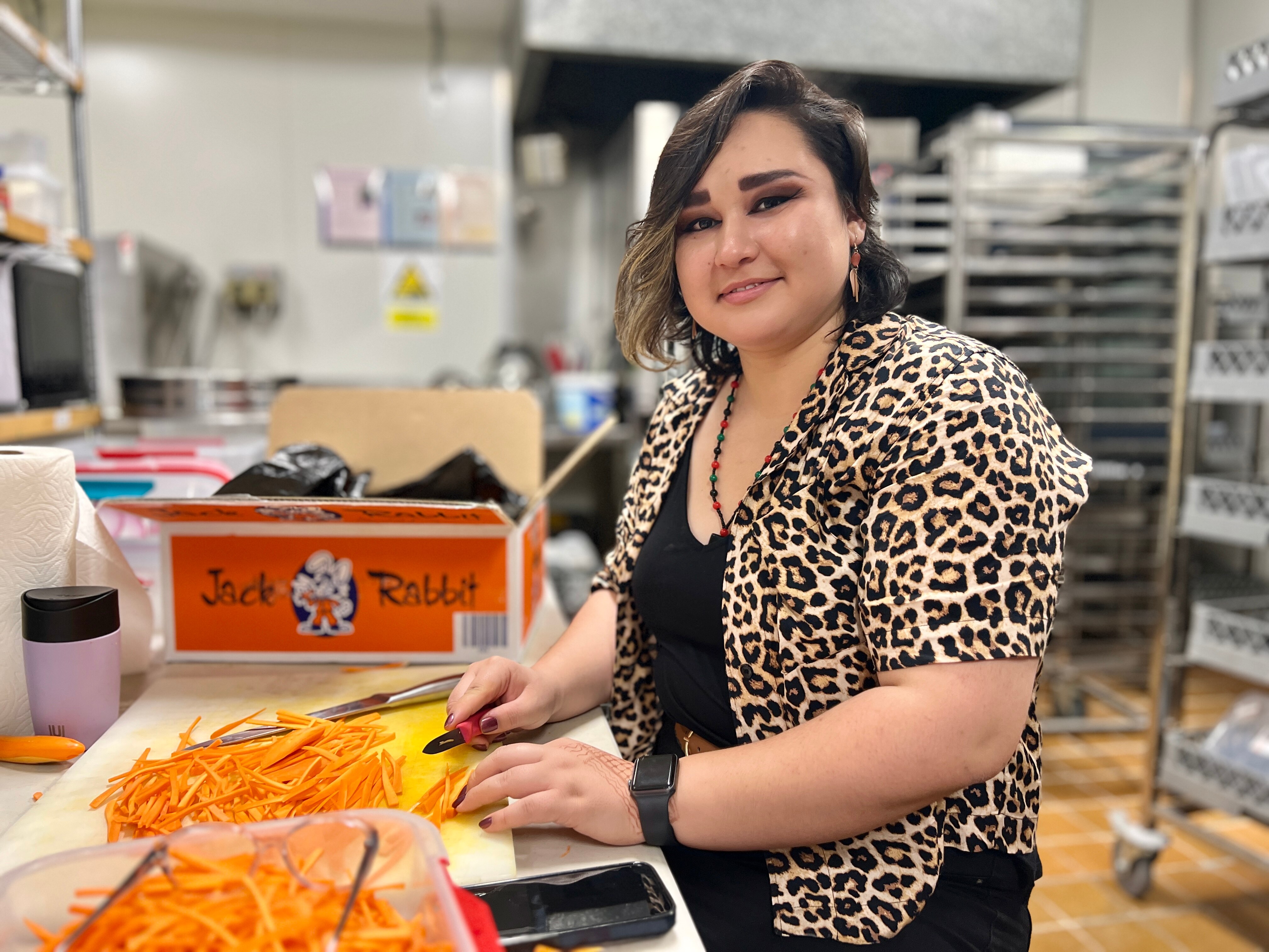 A woman smiles while cutting carrots