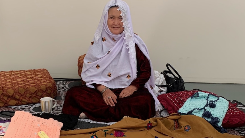 woman sitting on the ground with a headscarf and bags around her. 