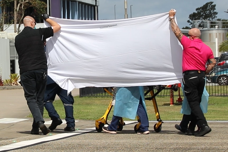Paramedics walking a wounded man on a gurney hidden behind a sheet