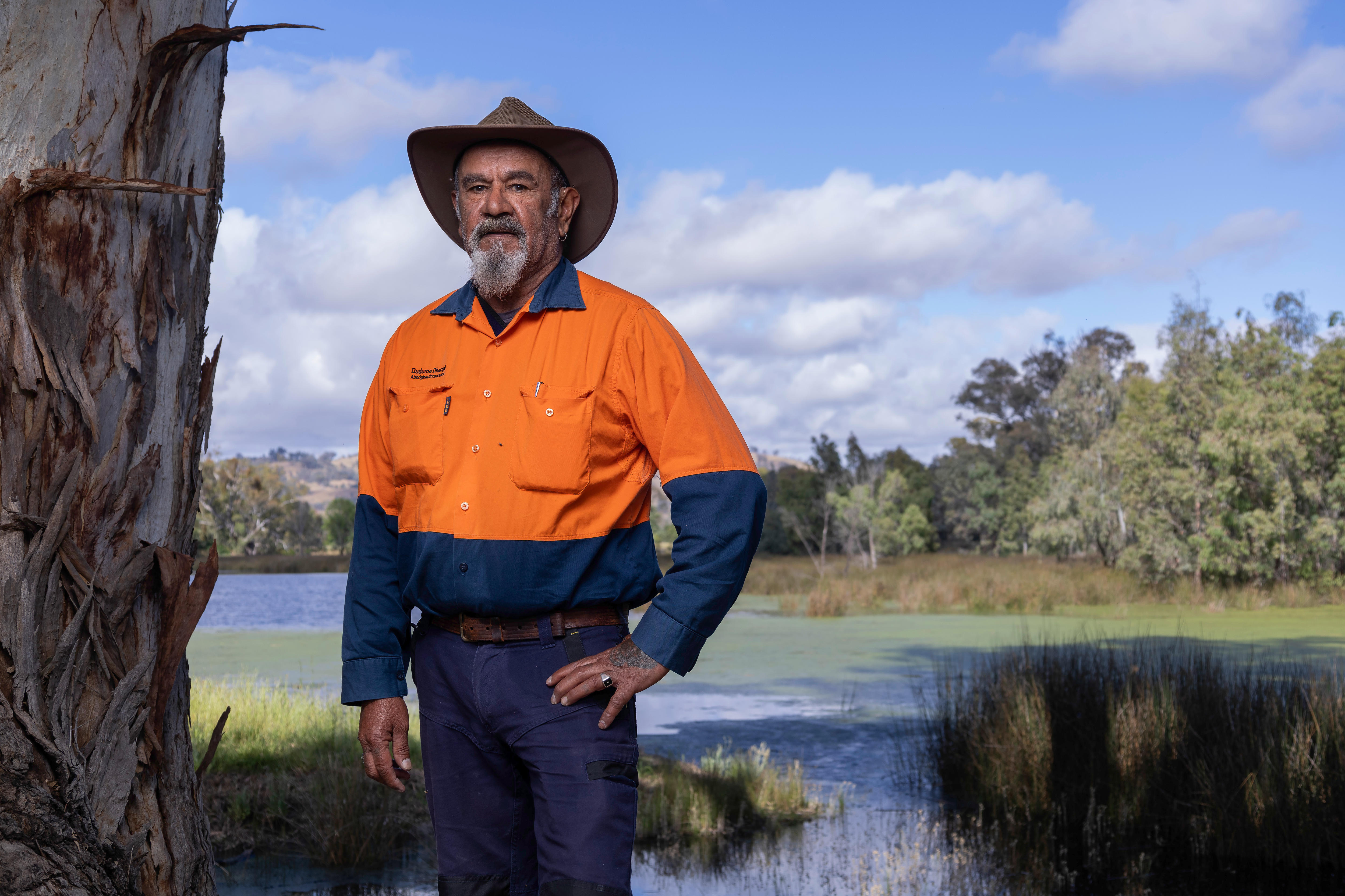 Un hombre vestido con una camisa de trabajo naranja de alta visibilidad se encuentra frente a un humedal. 