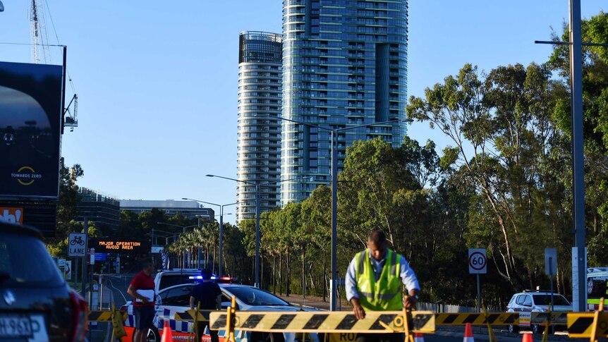 A large modern building can be seen behind a worker in a high-vis vest holding a road block