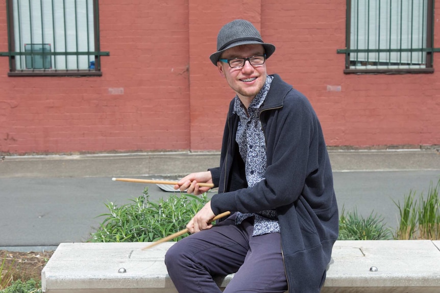 Jerrah Patston plays with his drum sticks on a park bench