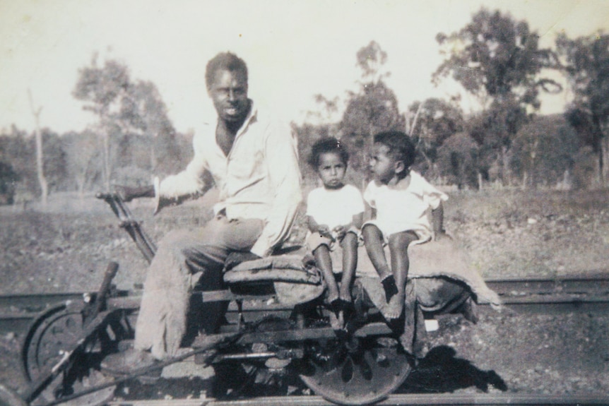 Photo d'archives en noir et blanc d'un insulaire du détroit de Torres sur un chariot à pompe avec ses deux enfants derrière lui. 