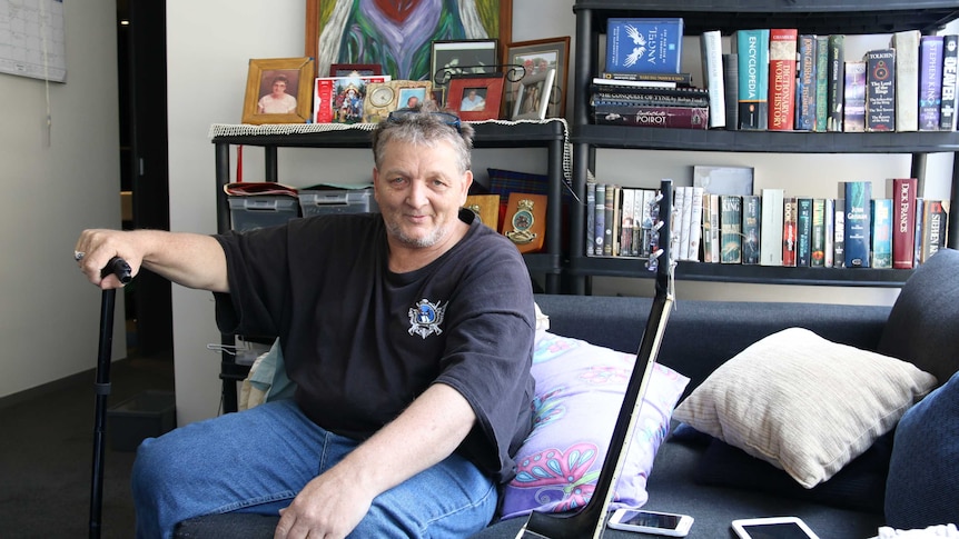 Robin Ford sitting on his lounge holding onto a walking stick.