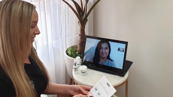 Nicole Bratis sits in front of a laptop at a beauty salon hosting a video call to a client.