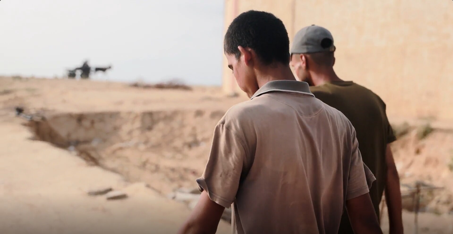The backs of two boys walking on a dirt path near a stone building