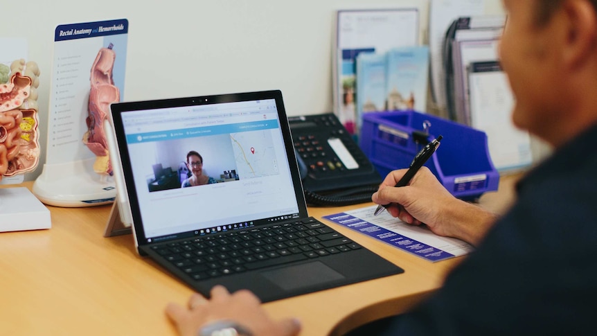 Man sits at desk looking at laptop screen, woman is displayed on screen