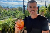 A man on a leafy rooftop holds up a spritz