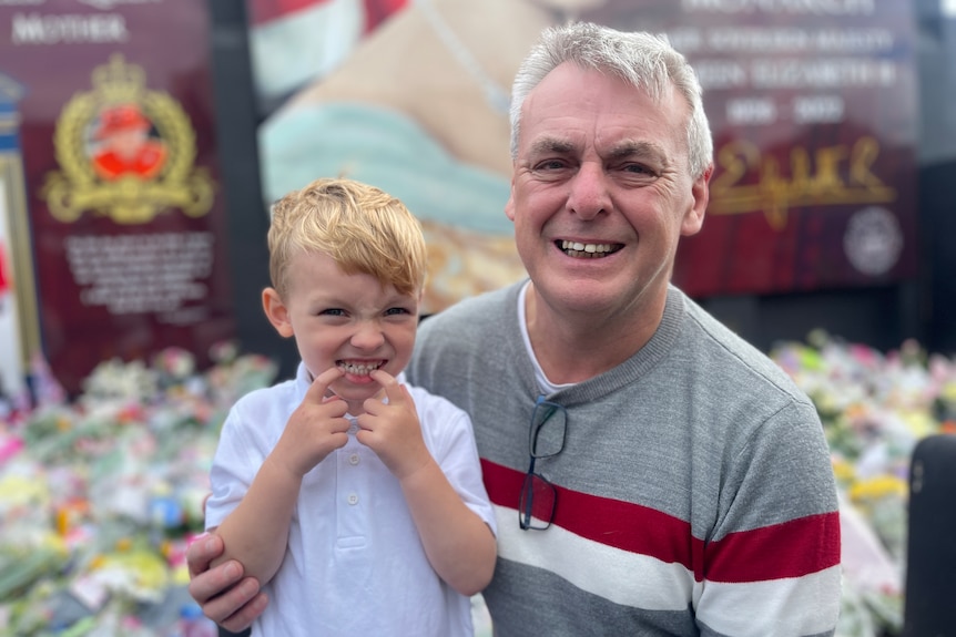 An older man with grey hair smiles and poses with his young grandson.