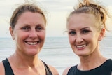 Two women stand on a beach smiling.