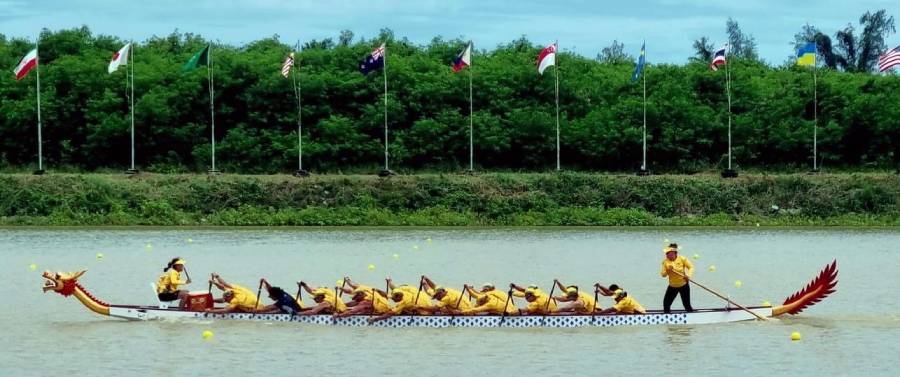 Women in yellow jerseys sit paddling in a long boat with a dragon's head at the front.