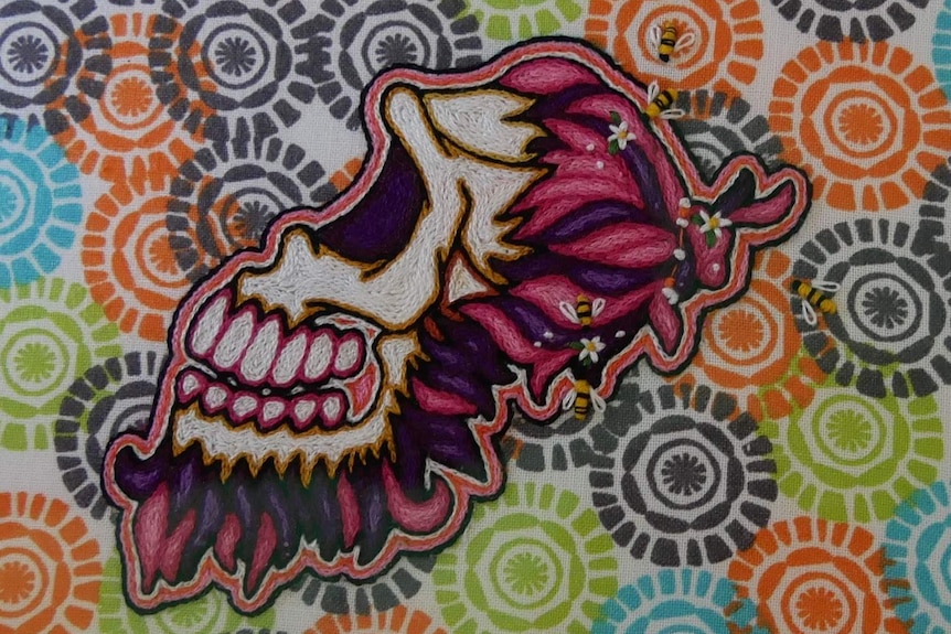 Brightly coloured skull made with tiny cross-stitch on bright fabric background