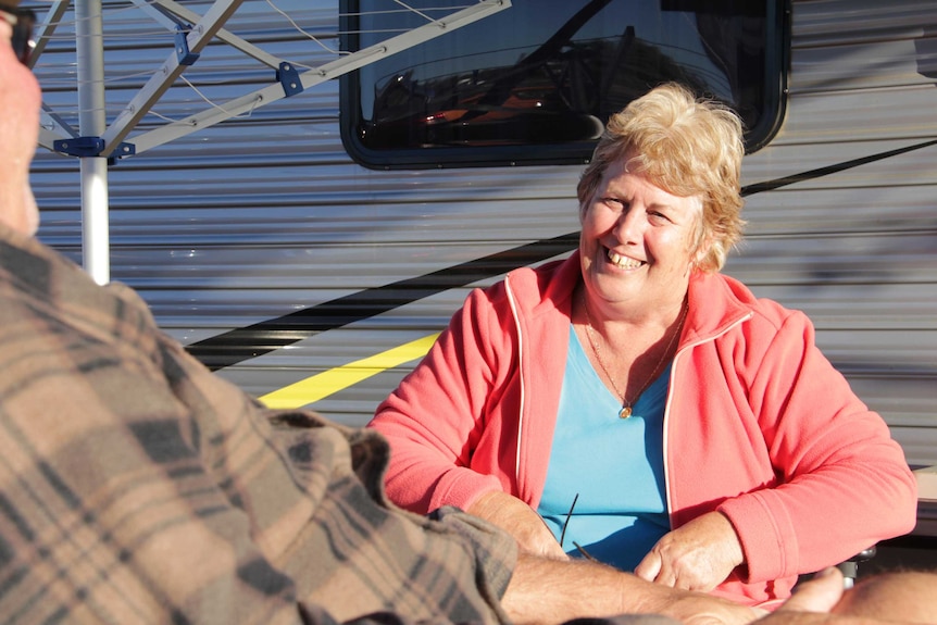 A woman in an orange jumper smiles broadly at a man outside a caravan.