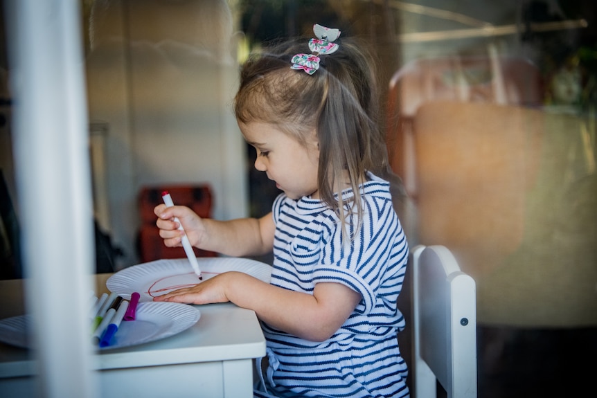 Emilia assise à une table dessine sur une assiette en carton.