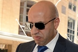 A man in sunglasses and suit leaves a court building