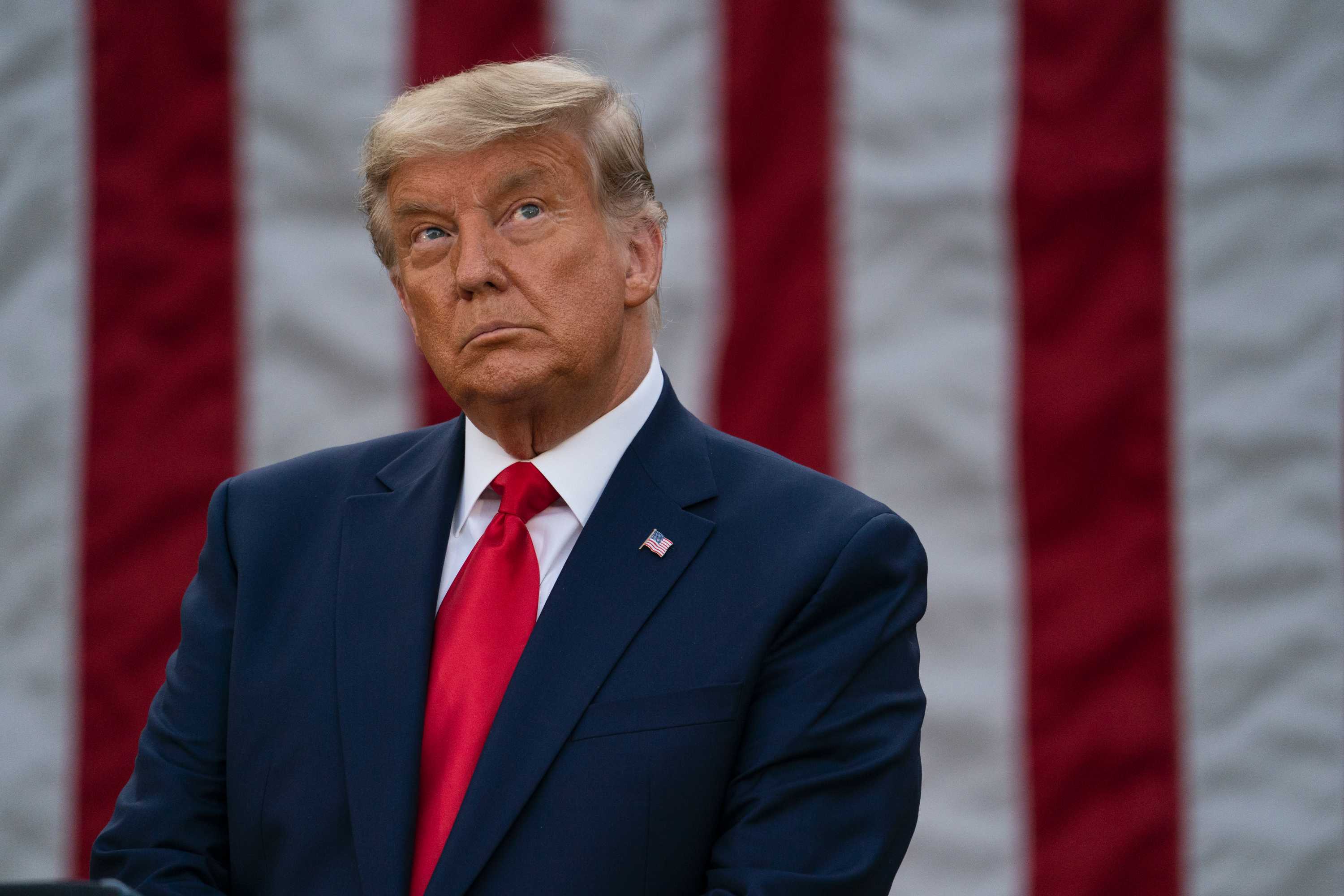 Donald Trump looks up during a pause at a media conference, in front of the American flag