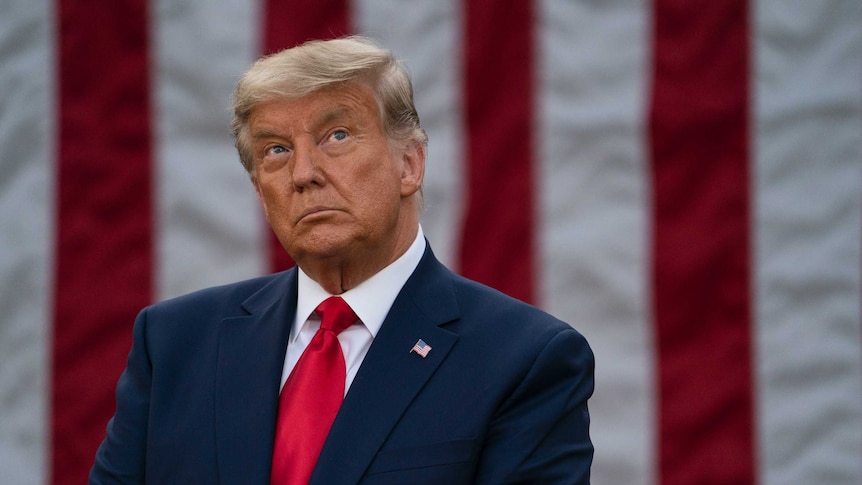 Donald Trump looks up during a pause at a media conference, in front of the American flag