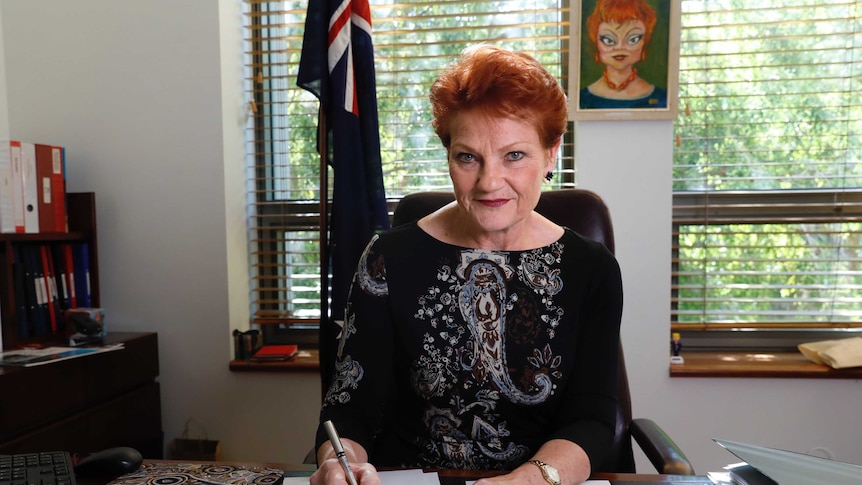 Middle aged woman sitting at desk with pen poised over papers.