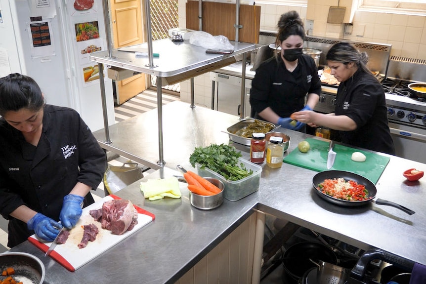 Three women dressed in black chef's uniform work in a commercial kitchen.