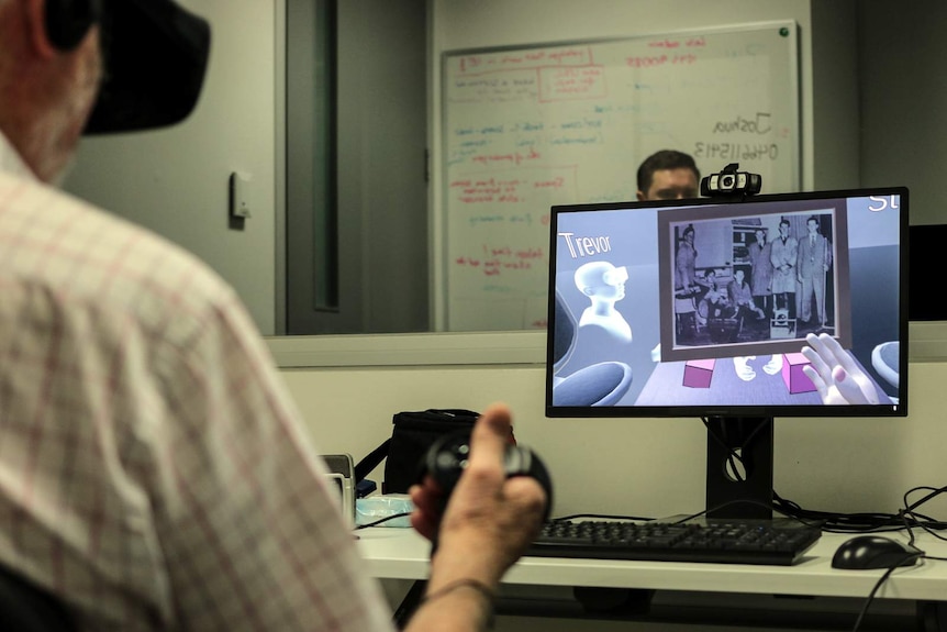 A man uses virtual reality as a computer screen shows a digitised photo of him in his high school years.