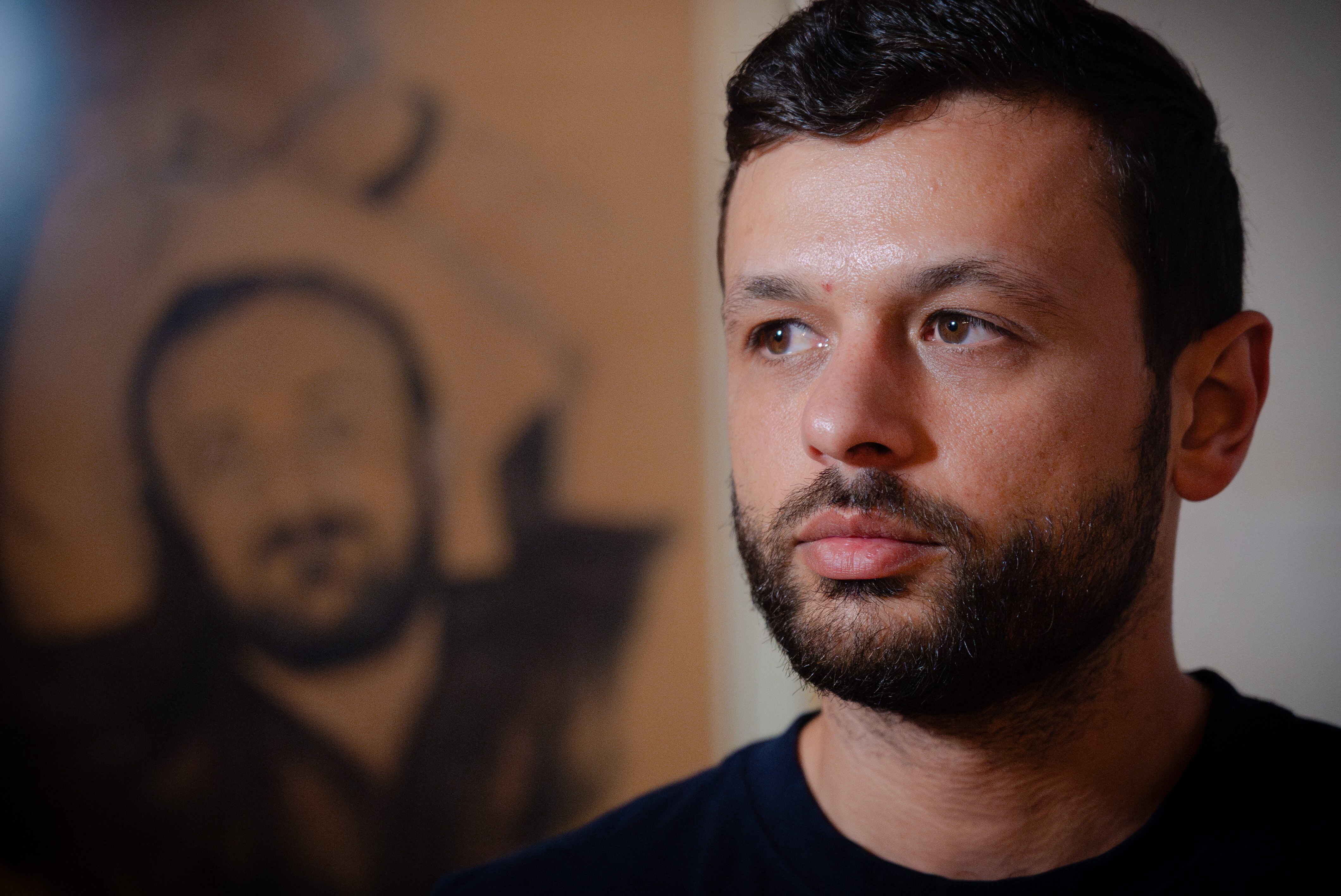 A young man looks solemn, a painting of Marwan Barghouti in handcuffs hangs on the wall behind him.