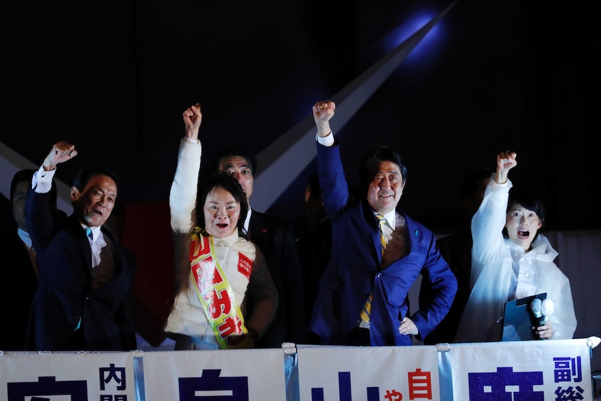 Four people stand with their arms raised to the crowd.