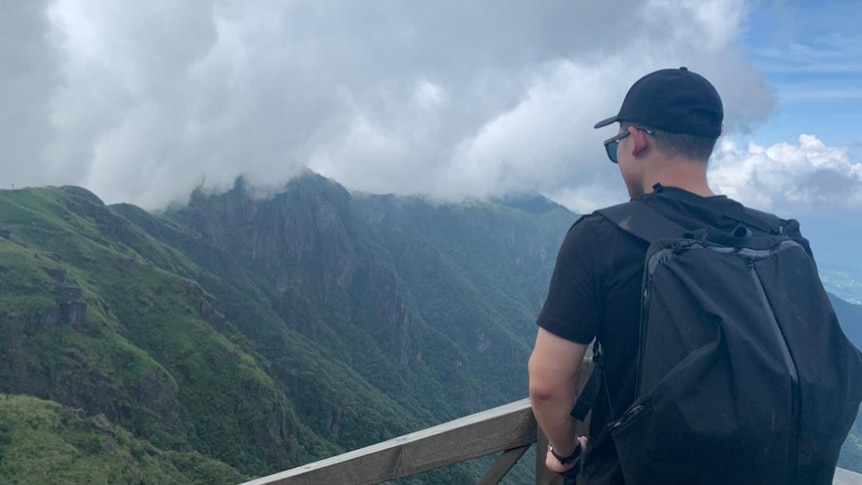 A young man is standing on the top of a mountain