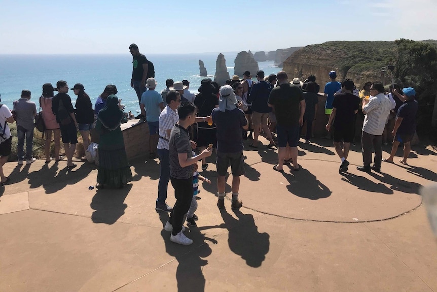 tourists gather along a clifftop looking at rock formations in the sea