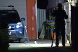 An area lit by a spotlight near a car in a driveway with a police officer taking photos.