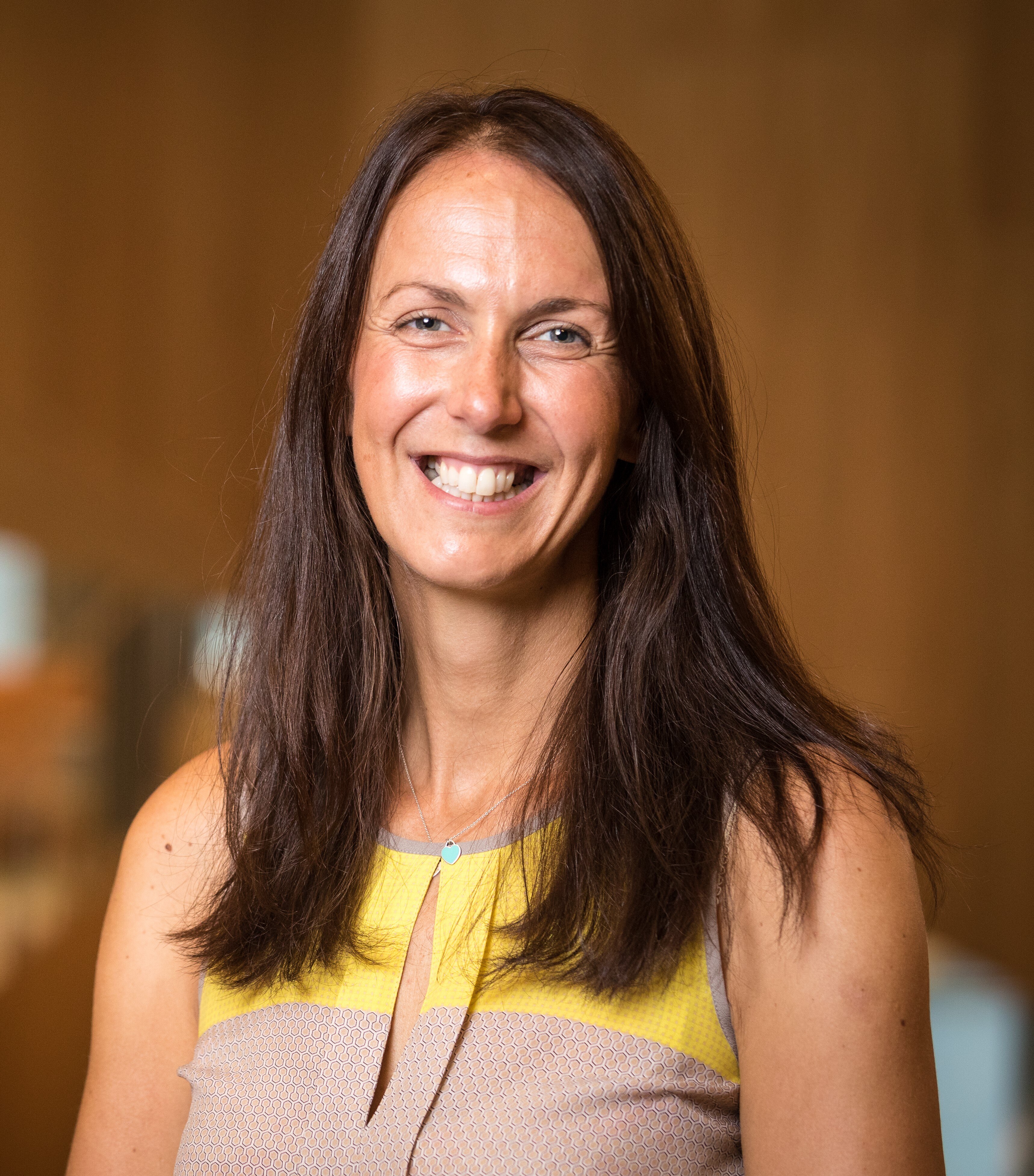 A profile shot of a woman with long brunette hair smiling at the camera. 