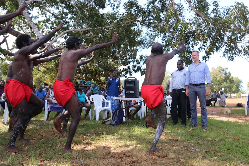Nigel Scullion watches a group of Indigenous men in traditional garments perform a ceremony dance.