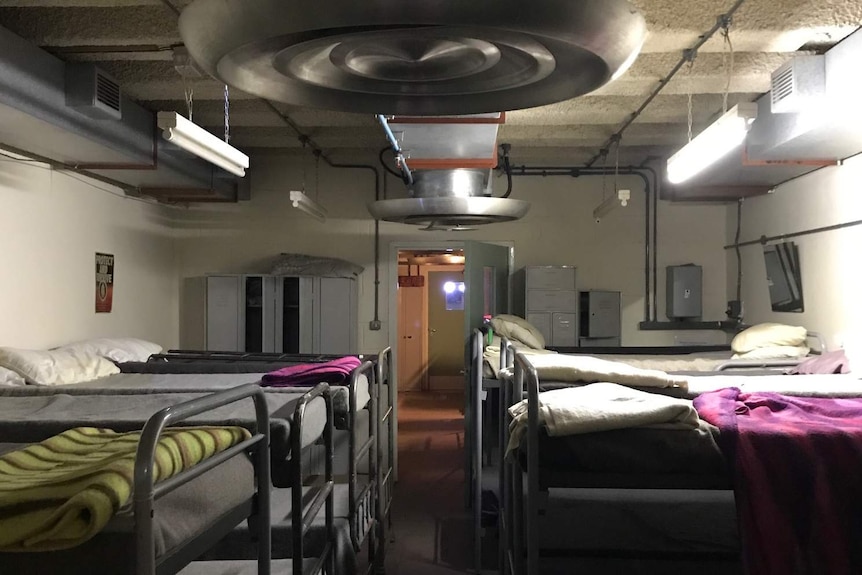 A concrete room underground with bunk beds.