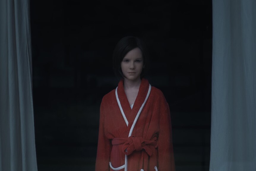 A young AI girl standing in a dressing gown in the film The Trouble with Being Born