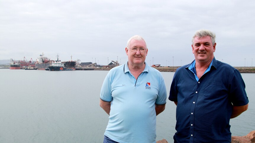 Dave Phillips and Brian Moncreiff stand at Port Kembla in front of the tug towing the Iron Chieftain.