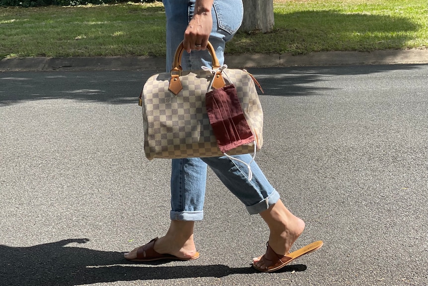 Lower half of woman while walking, carrying bag with mask attached