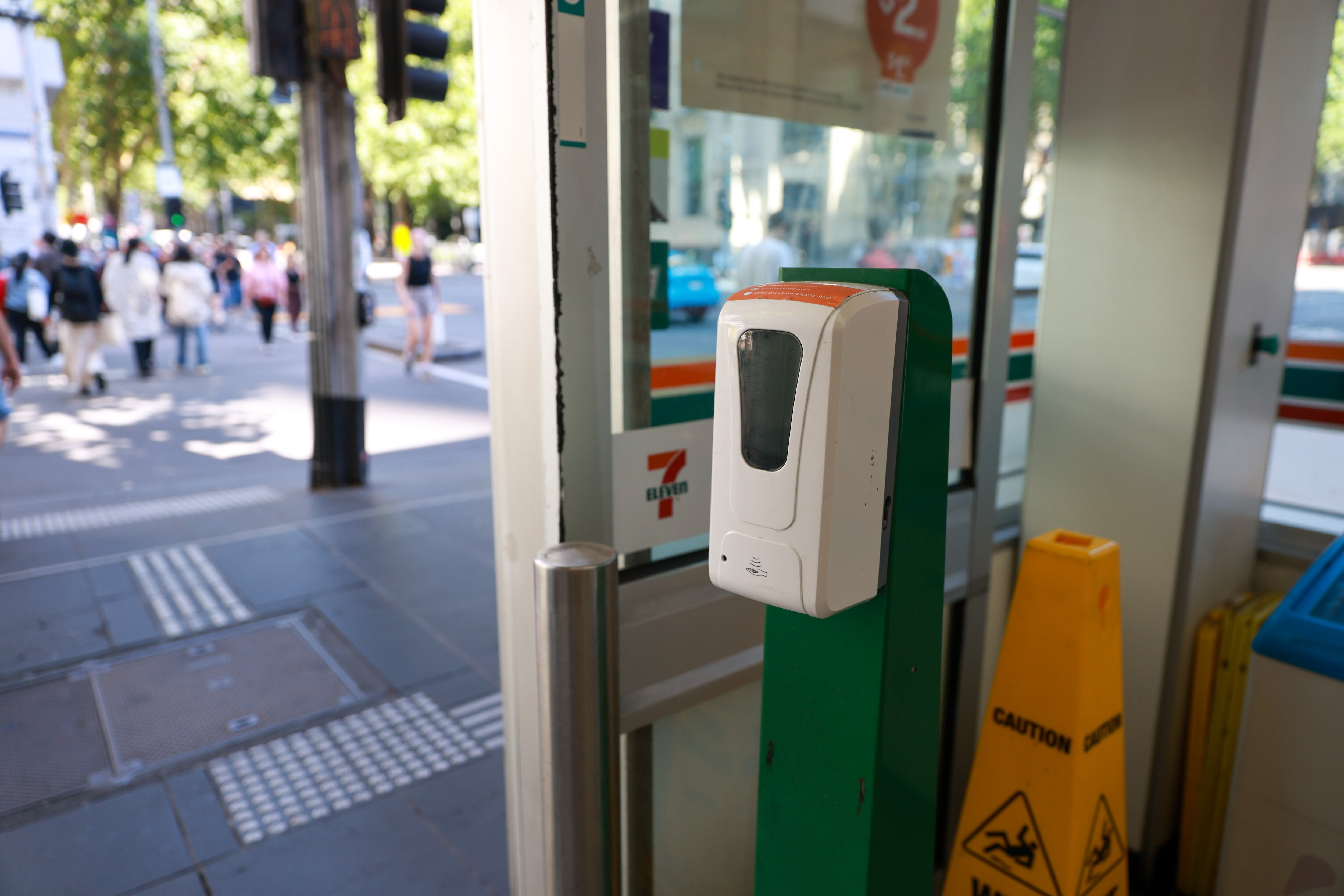 Faded social distance stickers on the footpath and people walking with masks as they pass hand sanitiser stations.