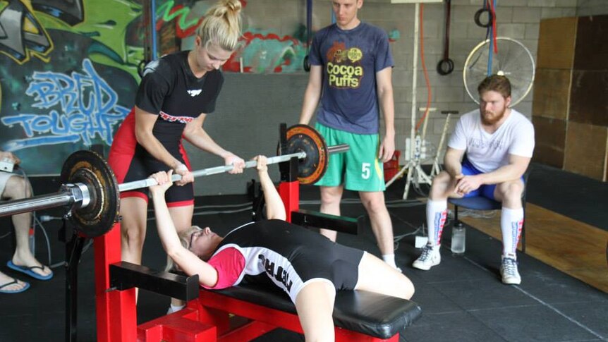 Daughter helps her mother benchpress weights at a Darwin gym