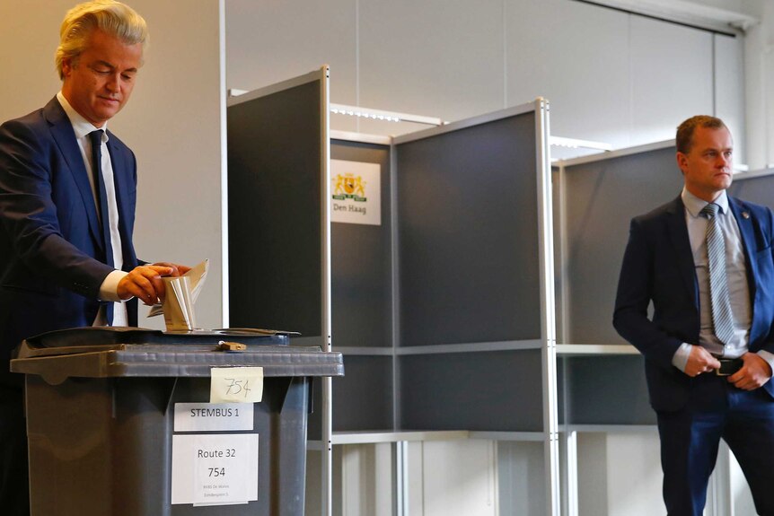 Geert Wilders places his vote into a ballot box as a security guard looks on