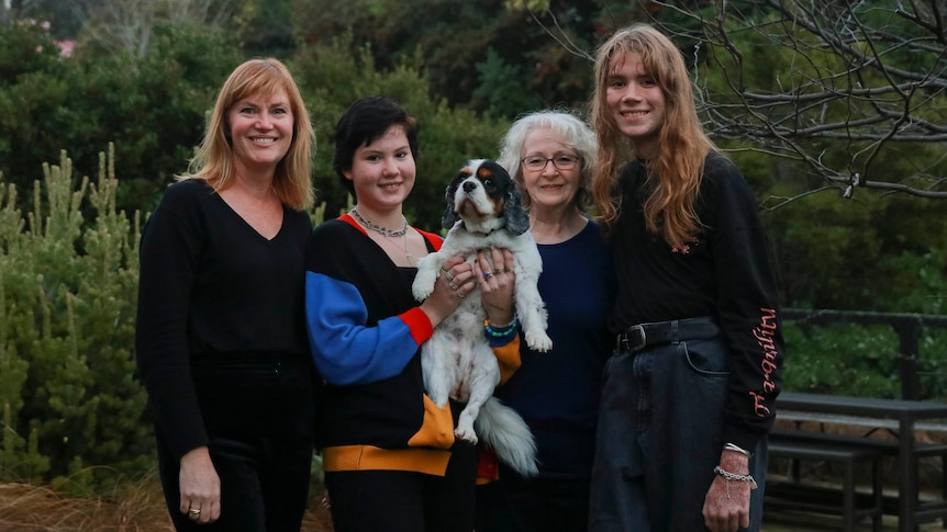 Four women and a dog standing next to each other.