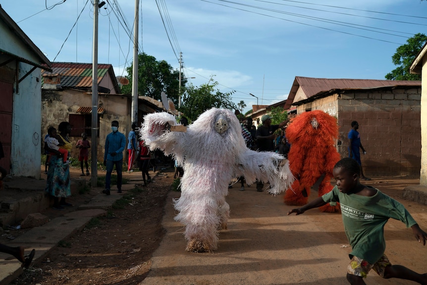A boy runs away from men dressed as Kankurang during a ritual procession in Bakau, Gambia