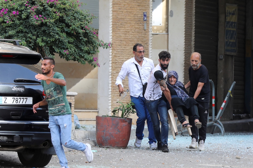 Three men carry an elderly woman out of a building on a chair as they evacuate following gunfire in Beirut.