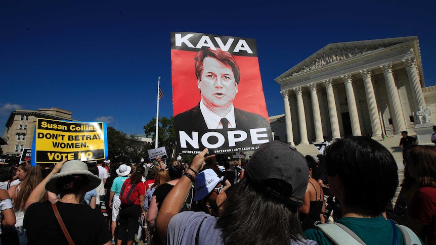 Protesters against Brett Kavanaugh demonstrate outside the Supreme Court. One is holding a sign that says "Kava Nope".