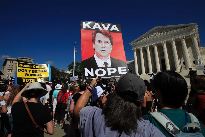 Protesters against Brett Kavanaugh demonstrate outside the Supreme Court. One is holding a sign that says "Kava Nope".
