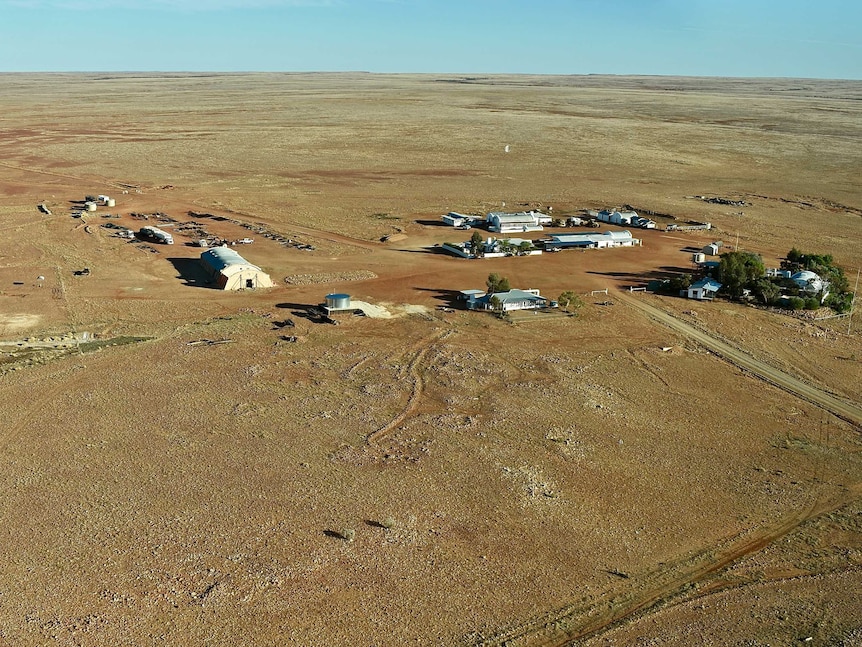 White and sandstone buildings sit in the middle of a flat open brown and orange outback plain