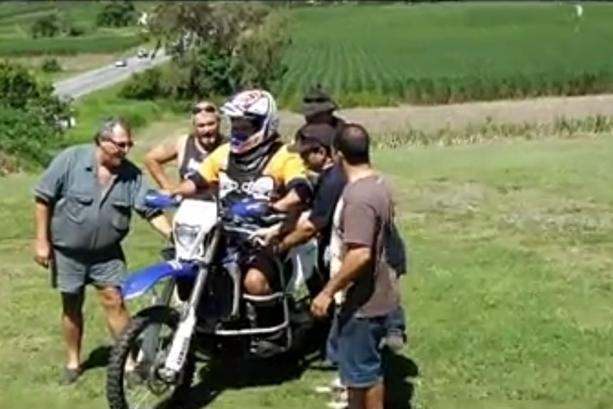 a group of people standing around a man on a dirt bike