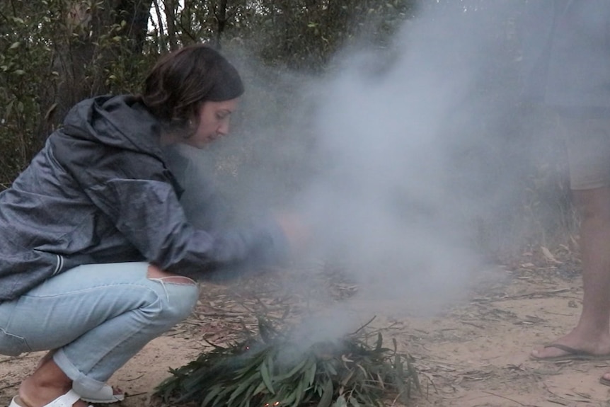 An Aboriginal woman ignites gum leaves to make a fire and smoke.