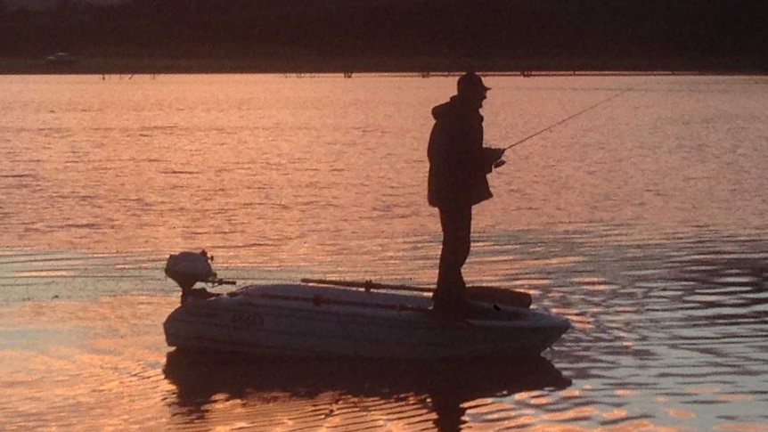 Andrew Caddle fishing standing up in his boat at sunset at Craigbourne Dam