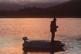 Andrew Caddle fishing standing up in his boat at sunset at Craigbourne Dam